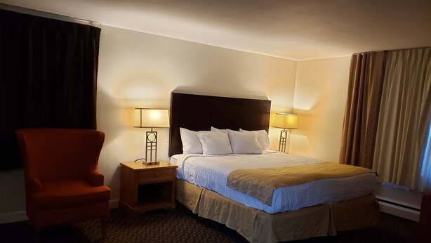 A hotel room with a large bed, two bedside lamps, a nightstand, a chair, and a carpeted floor. - Town & Country (Seekonk)