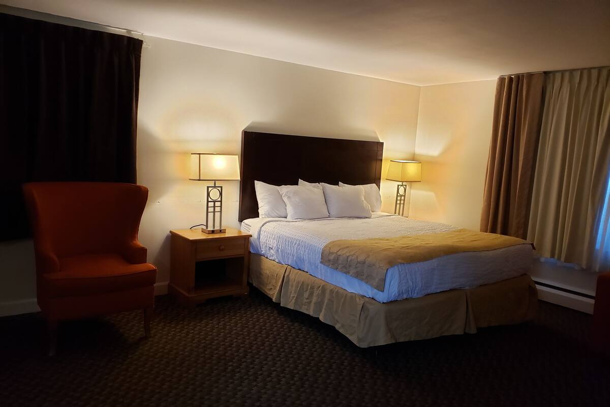 A hotel room with a large bed, two bedside lamps, a nightstand, a chair, and a carpeted floor.