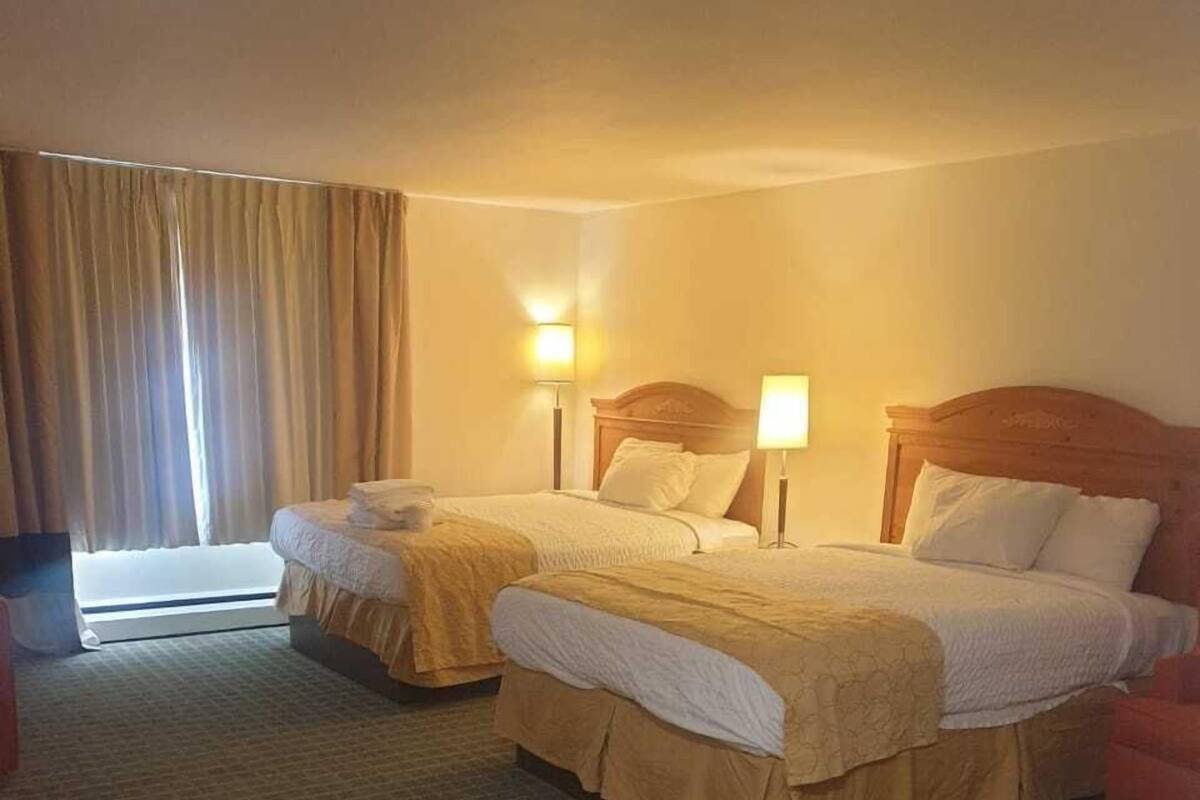A hotel room with two beds, a large window with curtains, and a carpeted floor.