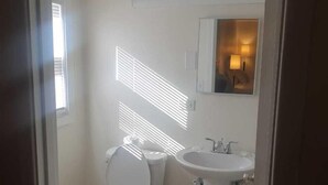A bathroom with a toilet, sink, and a mirror with a light fixture. - Town & Country (Seekonk)