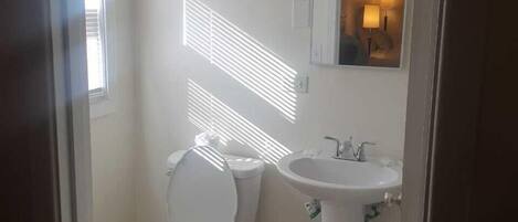 A bathroom with a toilet, sink, and a mirror with a light fixture.