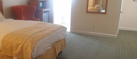 A hotel room with a large bed, a red chair, a small table with a television, and a mirror on the wall.