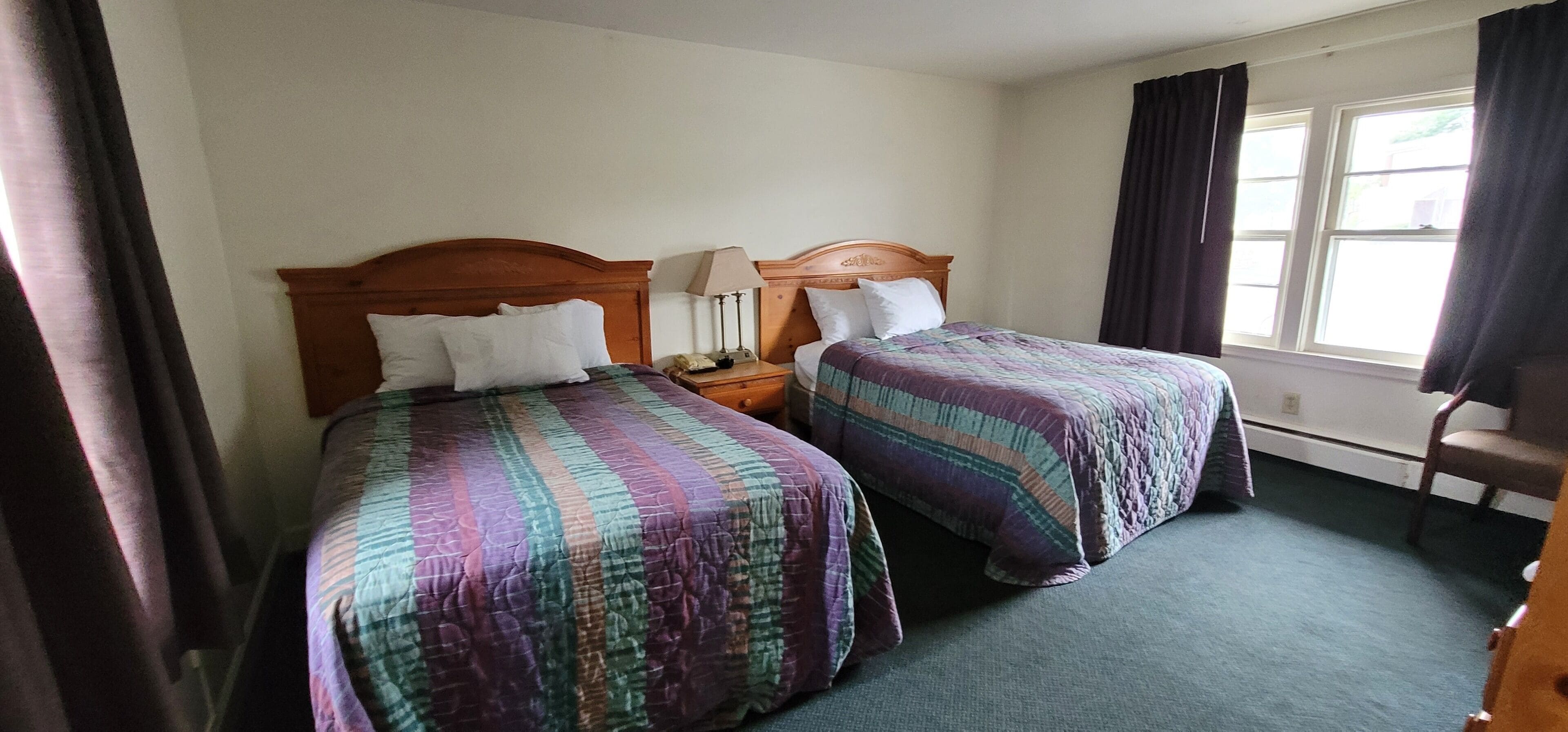 Una habitación de hotel con dos camas, una mesita de noche, una lámpara y una silla.