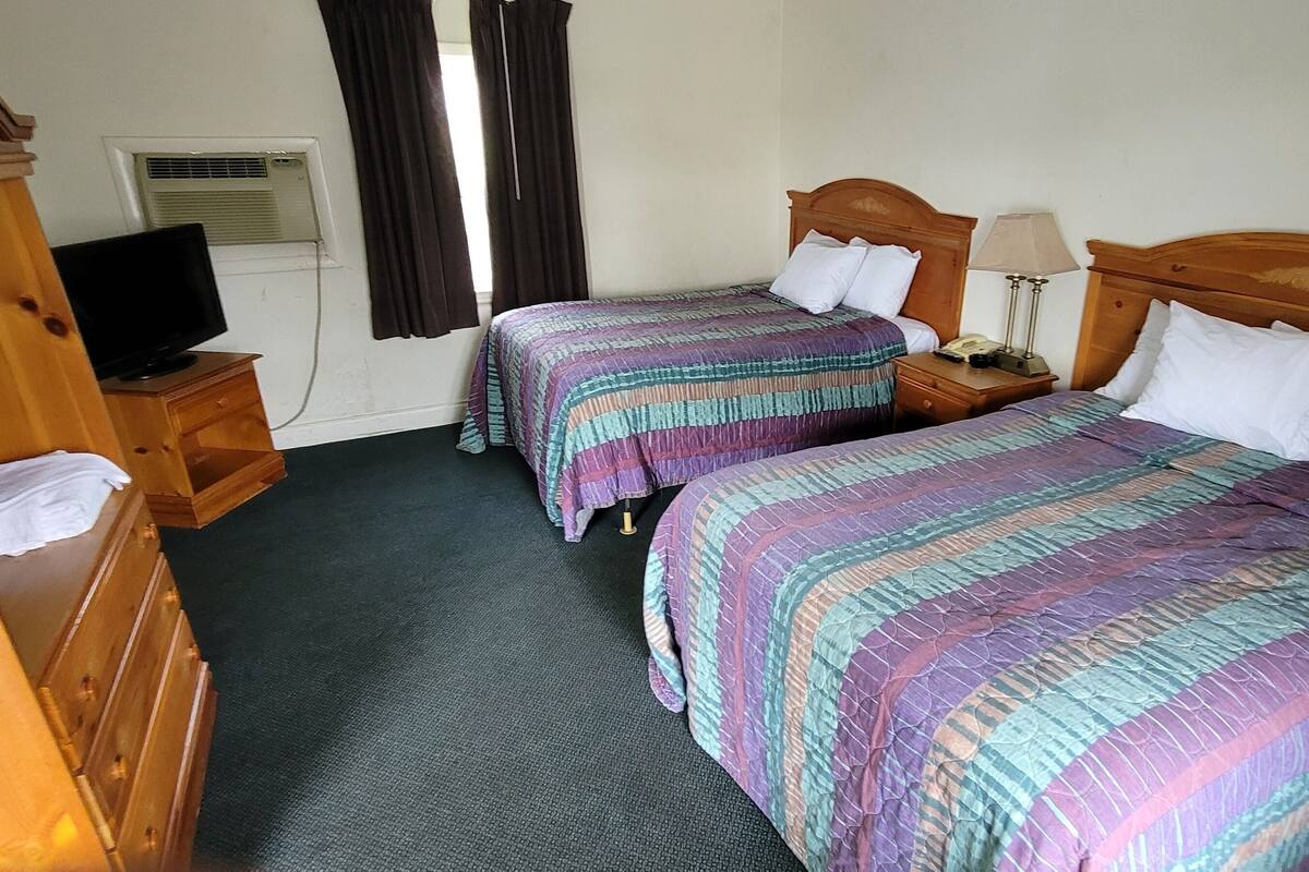 A hotel room with two beds, a television, a desk, and a window with curtains.