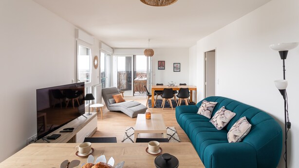 A modern living room with a teal sofa, wooden coffee table, and a flat-screen TV.