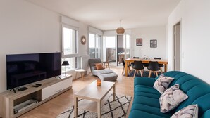 A modern living room with a flat-screen TV, a sofa, a coffee table, and a dining area with a table and chairs.