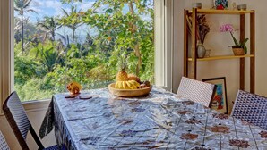 Une table à manger avec vue sur un paysage tropical, une petite table d’appoint en bois agrémentée d’objets décoratifs et une horloge murale.