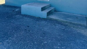 A single-story building with a white door, a small window, and a set of concrete steps leading to the entrance.