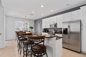 A modern kitchen with white cabinets, stainless steel appliances, and a central island with bar stools.