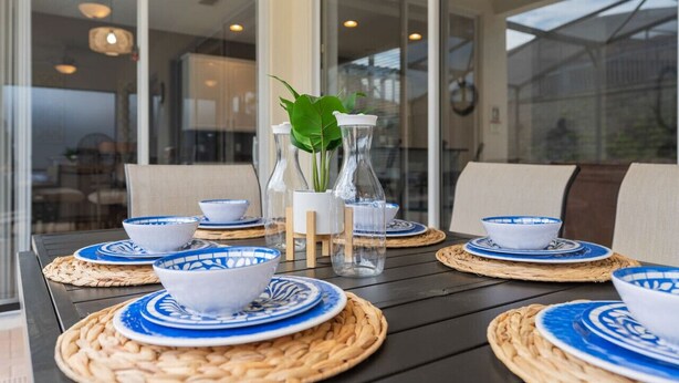 Een gedekte tafel met blauwe en witte borden, heldere glazen flessen en een potplant.