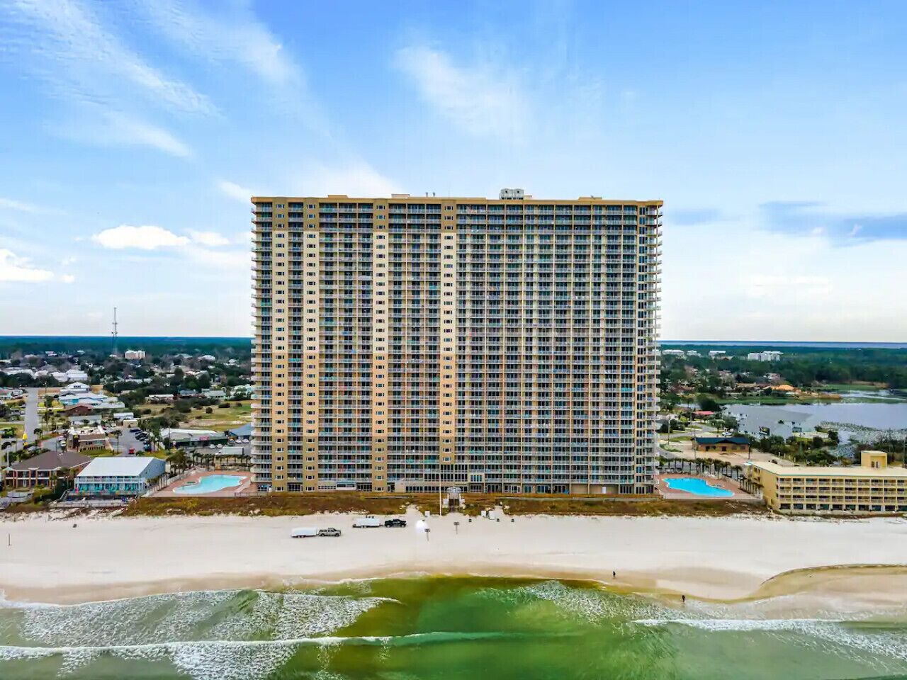 A high-rise hotel with a beach view, multiple balconies, and a pool area.