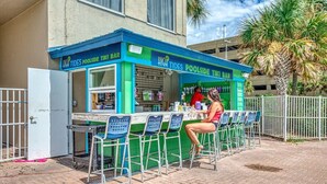 A beachside bar with a green and blue exterior, outdoor seating, and a view of palm trees. - Breathtaking Beachfront Condo, By Pier Park, Pools (Panama City Beach)