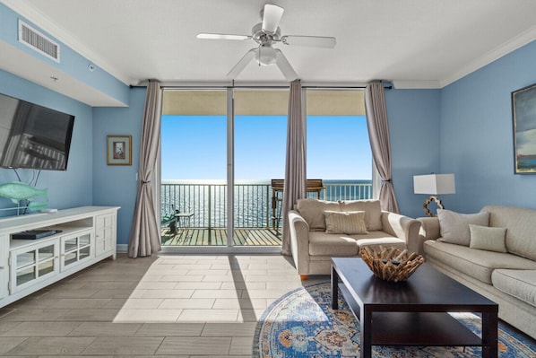 A spacious living room with a large window, a ceiling fan, a television, and a white entertainment unit.