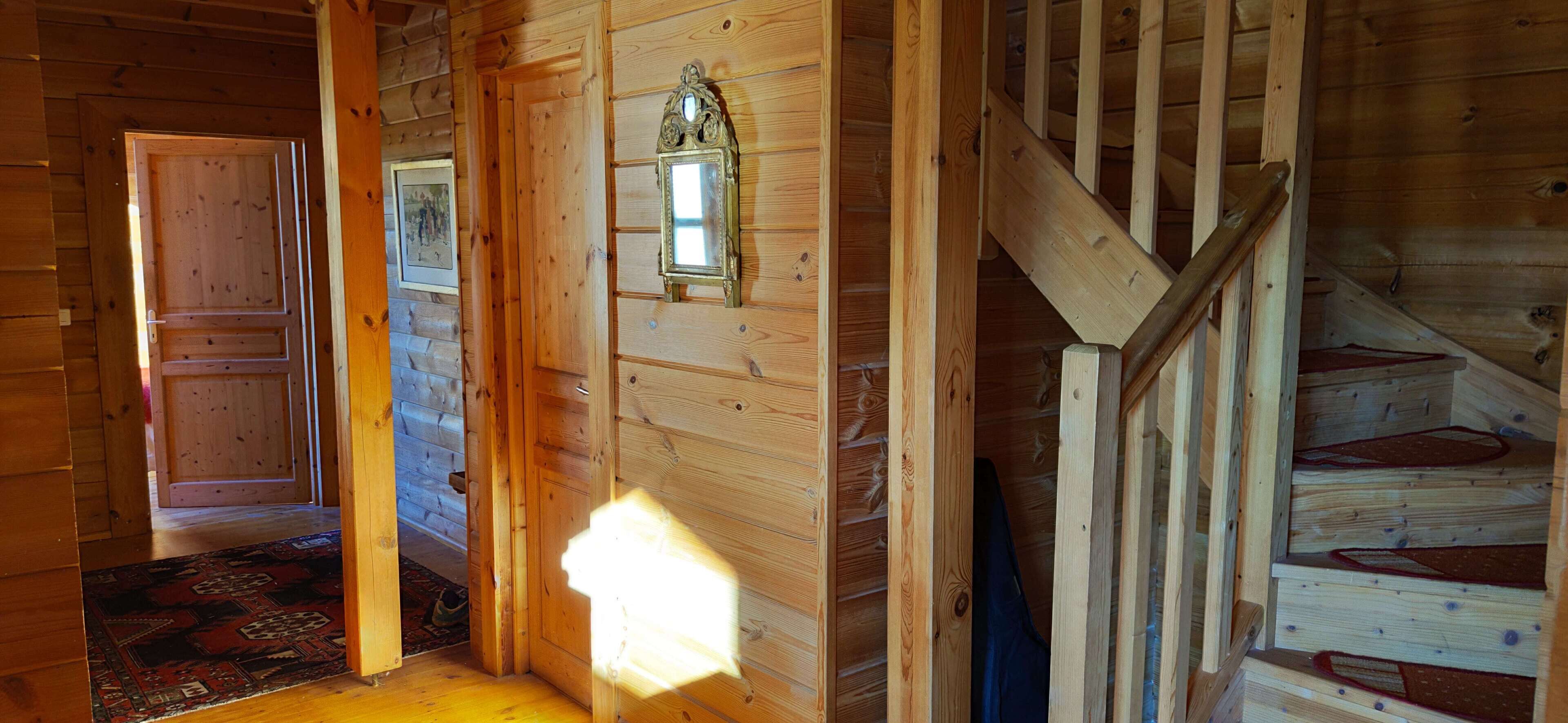 Un interior de fusta amb una escala, una porta i una làmpada penjada a la paret.