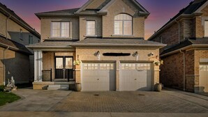 Une maison à deux étages avec une façade en briques, un porche à l’avant et deux portes de garage.