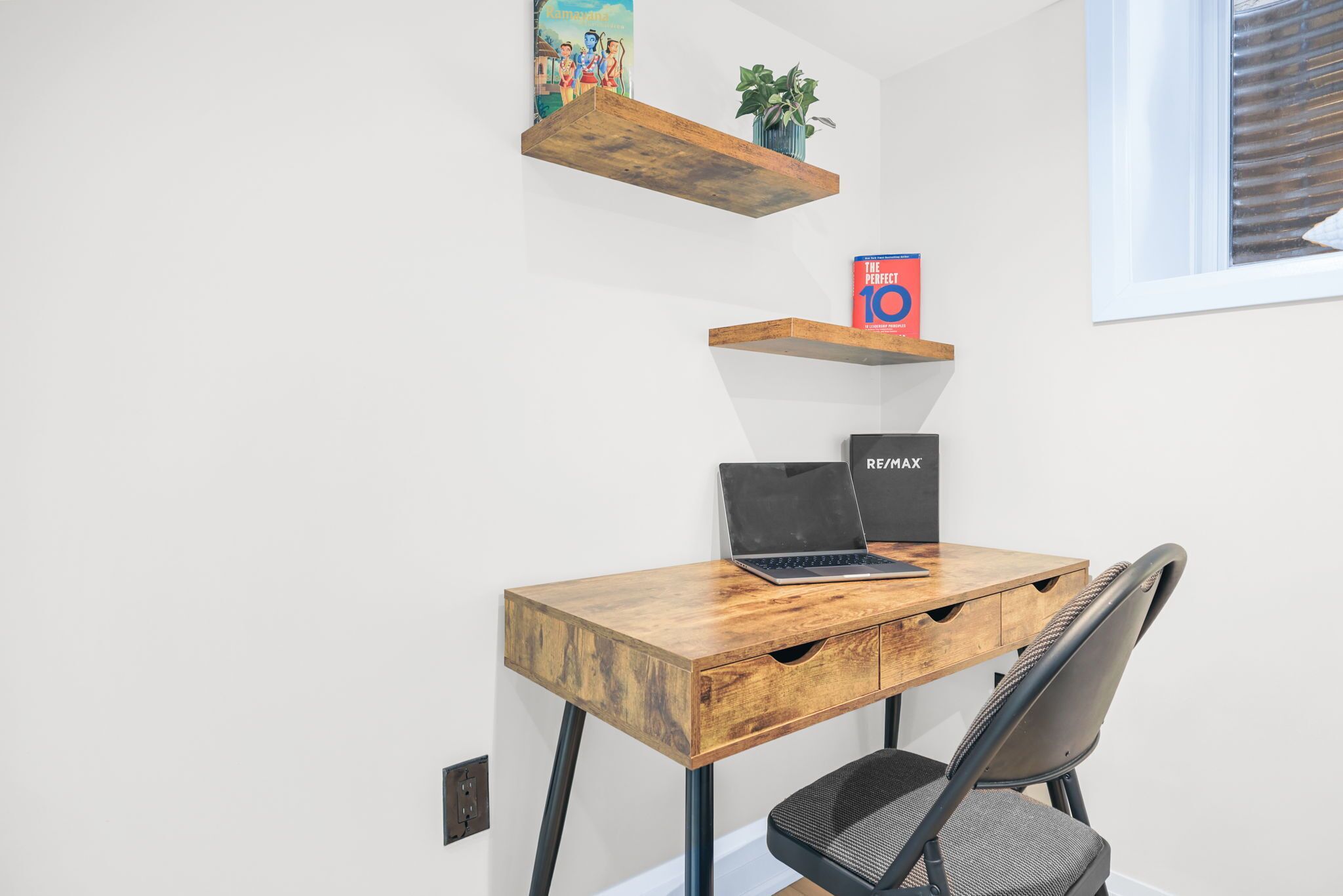 Un bureau en bois avec un ordinateur portable, une chaise et deux étagères murales où sont disposés des objets décoratifs.