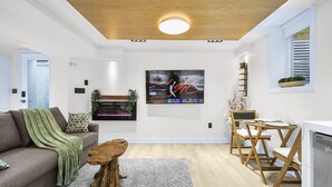 Un salon moderne doté d’un téléviseur à écran plat, d’une table basse en bois, d’un tapis gris et d’un coin repas avec des chaises en bois et une table blanche.