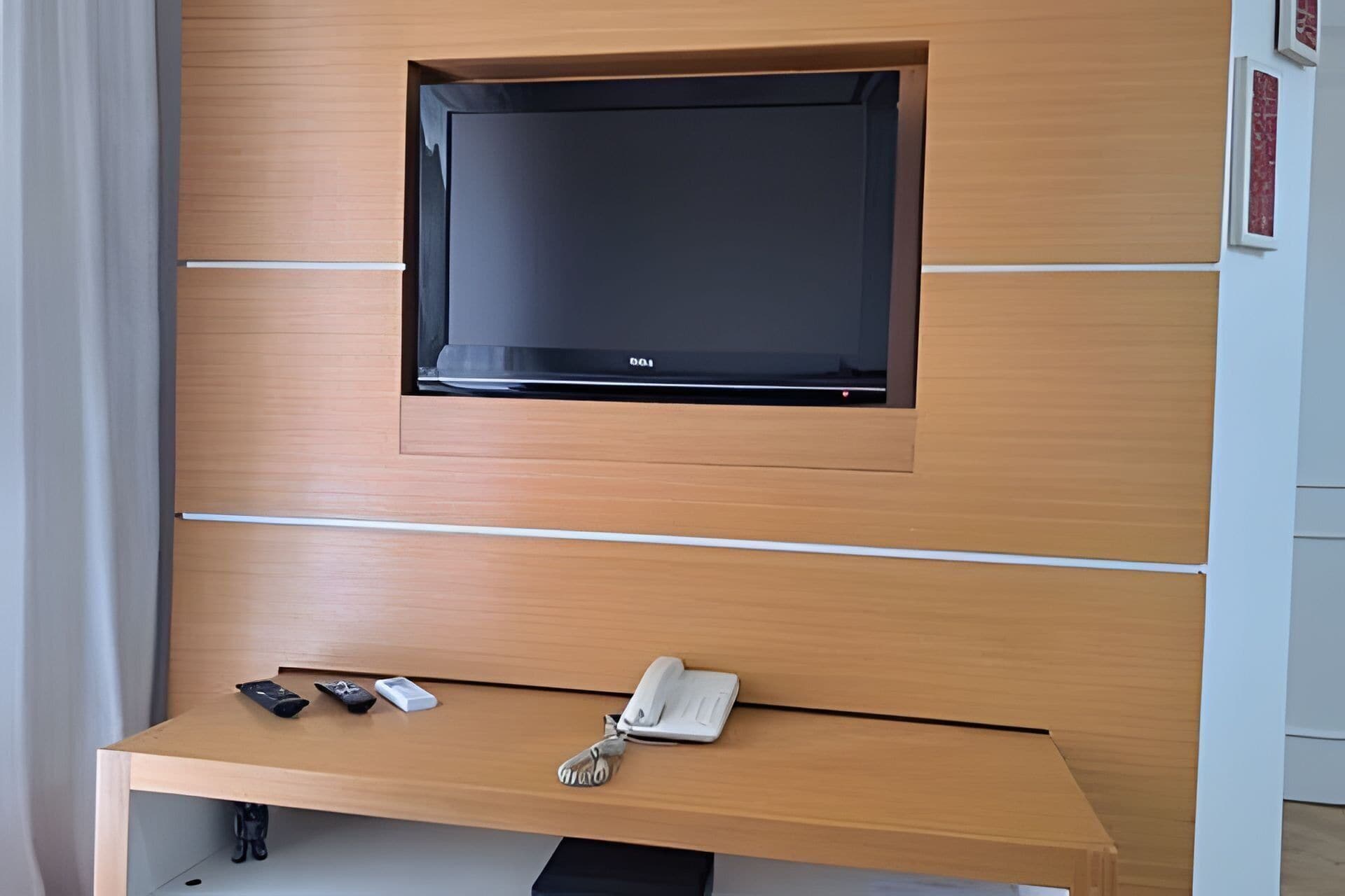 A modern room with a mounted TV on a wooden wall, a small desk with a telephone, and some personal items.