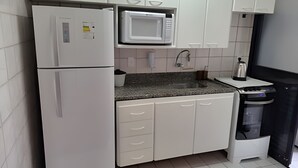 Eine kleine Küche mit weißen Schränken, einer eingebauten Mikrowelle, einem Kühlschrank, einer Spüle und einem Mülleimer.