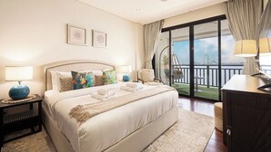 Une chambre d’hôtel avec un grand lit, un bureau, une chaise, un balcon avec vue et deux tableaux encadrés au mur.