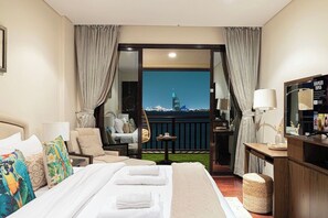 Een hotelkamer met een bed, een stoel, een tafeltje, een televisie en uitzicht op een stadsbeeld.