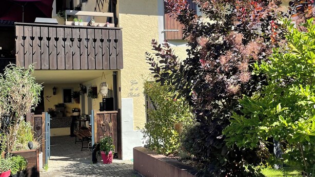 A two-story building with a balcony, a wooden fence, and potted plants.
