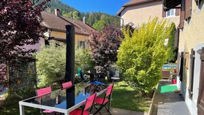 An outdoor patio with a table and chairs, surrounded by greenery and a view of a mountain.
