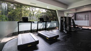 Een moderne sportschool met loopbanden, krachttoestellen en een groot raam met uitzicht op bomen.