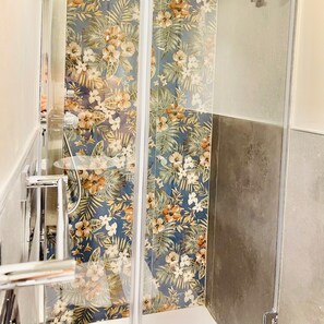 Une douche dotée d’une porte en verre ornée de motifs floraux, d’un pommeau de douche en métal et d’un mur carrelé.
