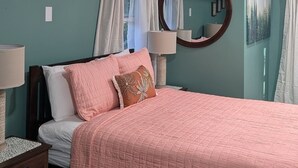 Een slaapkamer met een bed, nachtkastje, lamp, spiegel en een raam met gordijnen.