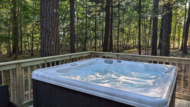 Een hottub op een houten terras, omringd door een bos.