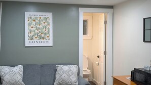 A room with a grey sofa, wooden dresser, and a poster on the wall. - New Cabin for your Holiday_Cabin 12B (Bar Harbor)