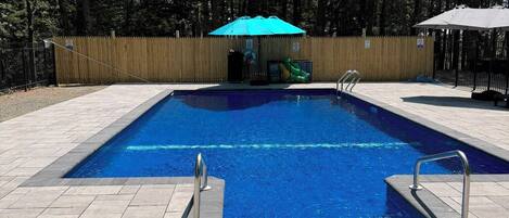 En rektangulär swimmingpool med blått kakel på insidan, omgiven av en stenlagd poolterrass. Det finns två metallstegar på vardera sidan.