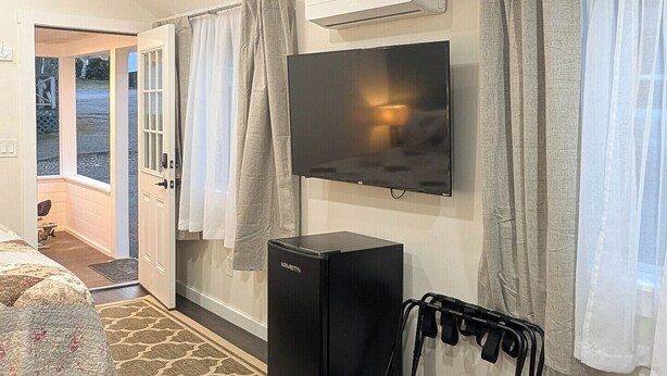 A hotel room with a bed, a TV, a small black refrigerator, a treadmill, and an air conditioning unit. - New Cabin for your Holiday_Cabin 12B (Bar Harbor)