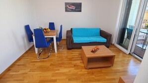 Una sala de estar moderna con piso de madera, un sofá azul, una mesa de centro de madera y un comedor con sillas y mesa azules.