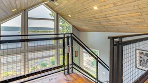 Eine Holzbalkendecke mit Deckenventilator, große Fenster mit Seeblick und ein Metallgeländer.