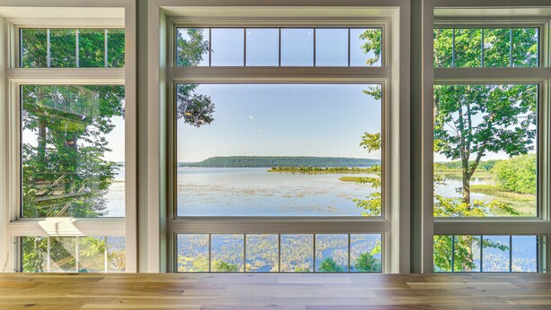 Ein Zimmer mit großen Fenstern und Blick auf einen See und Bäume.