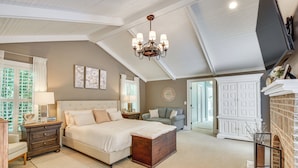 A bedroom with a large bed, a chandelier, a dresser, and a fireplace. - Spacious Taylors Home ~ 5 Mi to Dtwn Greenville! (Taylors)