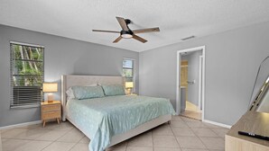 A bedroom with a bed, nightstands, a ceiling fan, and a door leading to a bathroom.