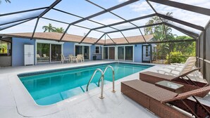 A pool area with a clear view of the pool, lounge chairs, and a covered patio.