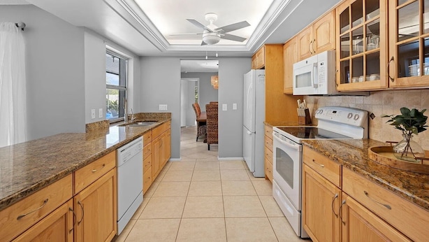 A modern kitchen with granite countertops, wooden cabinets, a built-in microwave, and a ceiling fan.