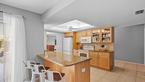 A modern kitchen with a central island, bar stools, wooden cabinets, and a microwave.