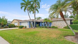 A two-story house with a stone facade, a garage, and a well-maintained lawn with palm trees.