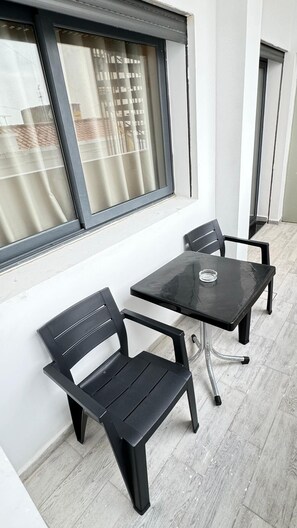 Ein kleiner Außenbereich mit Tisch und zwei Stühlen, neben einem Fenster mit Blick auf Gebäude.