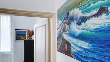 Un corridoio con un quadro che raffigura un paesaggio costiero incorniciato e una porta che dà su un'altra stanza.