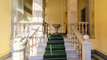 A grand staircase with marble steps and wooden balustrades, leading to a bright interior space.