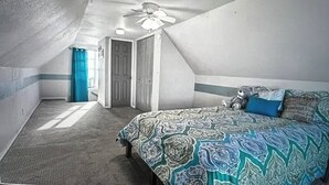 A bedroom with a patterned bedspread, a ceiling fan, and a door leading to another room.