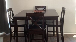 A dining area with a dark wooden table and four chairs, a framed artwork above the table, and a window on the left side.