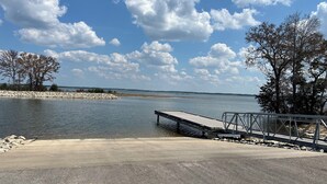 A concrete dock extending into a calm lake, surrounded by trees and a rocky shoreline.
