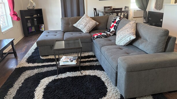 A living room with a grey sectional sofa, a glass coffee table, and a black and white rug.